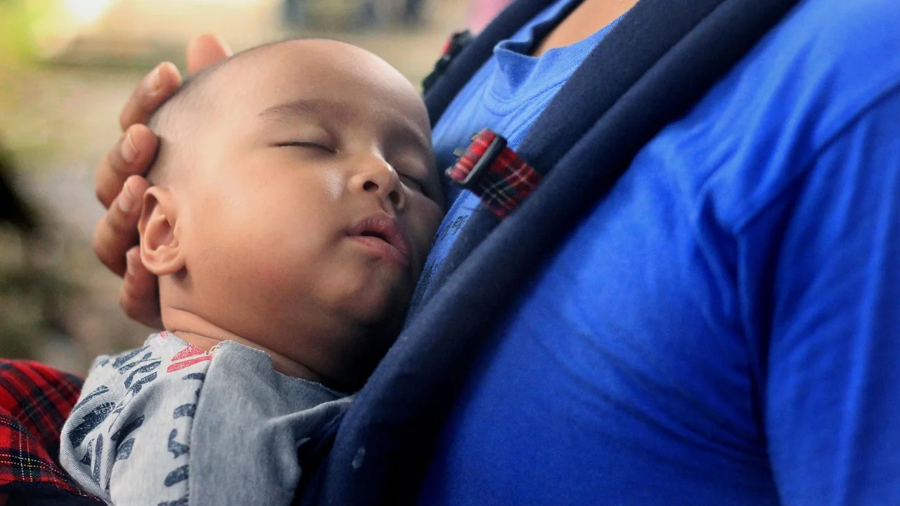 Un bébé endormi dans un porte-bébé, la joue contre son parent, le visage dégagé