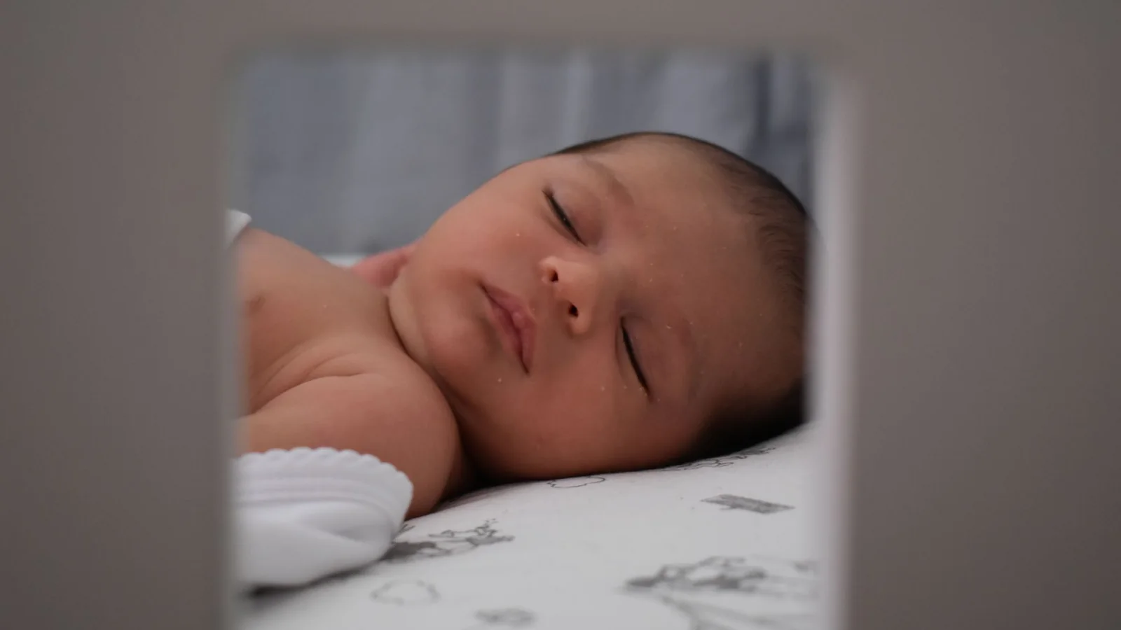 Un bébé endormi sur le dos dans son lit, vu entre les barreaux, sur un simple drap-housse